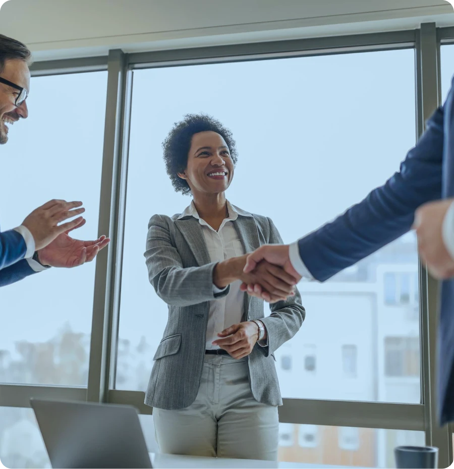 mulher de terno apertando as mãos de outra pessoa de terno, simbolizando uma reunião, negócio bem feito